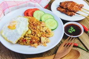 nasi goreng riso fritto pollo con uovo pomodoro cetriolo su piatto bianco e satay con salsa - nasi goreng ayam cibo indonesiano asiatico foto