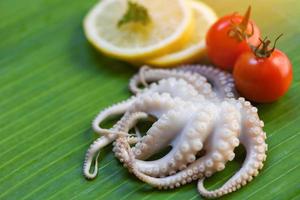 frutti di mare fresco calamaro polpo crudo e Limone prezzemolo pomodoro su Banana foglia sfondo foto