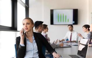 attività commerciale donna parlando su Telefono a ufficio con squadra su incontro nel sfondo foto