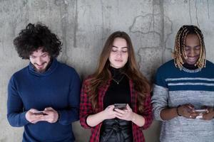 casuale multietnico attività commerciale squadra utilizzando mobile telefoni nel davanti di un' calcestruzzo parete foto