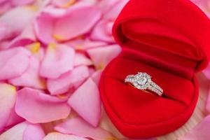 elegante anello di diamanti da sposa in scatola di gioielli a cuore rosso su uno sfondo di petali di rosa rosa bellissimo primo piano foto