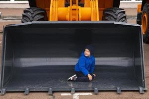 Minsk, bielorussia, settembre 20, 2022- bambino, ragazzo in posa dentro secchio di escavatore, strada auto caricatore foto