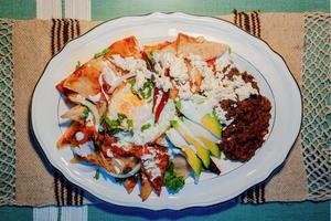 chilaquiles messicano cibo con nel rosso salsa, formaggio, crema e chili peperoni su Vintage ▾ sfondo foto