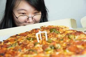 occhiali asiatici giovane donna apre la scatola della pizza ed eccita per la pizza di grandi dimensioni che contiene. riprese in studio di luce. foto