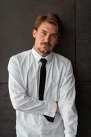 ritratto di avviare uomo d'affari nel un' bianca camicia con un' nero cravatta in piedi nel davanti di grigio parete al di fuori foto