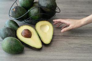 donna mano con tagliare metà, affettato fresco verde avocado su Marrone di legno tavolo. frutta salutare cibo concetto. foto