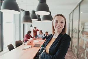 ritratto di contento donna d'affari proprietario nel moderno ufficio. donna d'affari sorridente e guardare a telecamera. occupato diverso squadra Lavorando nel sfondo. comando concetto. testa sparo. foto