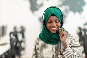 afro musulmano femmina con verde hijab sciarpa cliente rappresentante attività commerciale donna con Telefono cuffia porzione e supporto in linea con cliente nel moderno chiamata centro foto