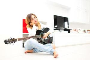 bellissimo donna nel casa seduta su il pavimento con sua mancino chitarra foto