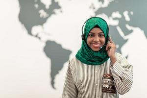 afro musulmano femmina con verde hijab sciarpa cliente rappresentante attività commerciale donna con Telefono cuffia porzione e supporto in linea con cliente nel moderno chiamata centro foto