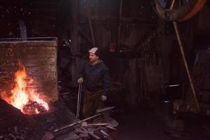 giovane tradizionale maniscalco Lavorando con Aperto fuoco foto