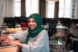 africano musulmano attività commerciale donna indossare un' verde hijab e Lavorando su il computer portatile computer nel rilassamento la zona a moderno Aperto Piano avviare ufficio. foto