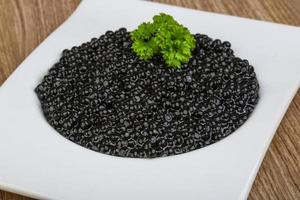 caviale nero in una ciotola su fondo di legno foto