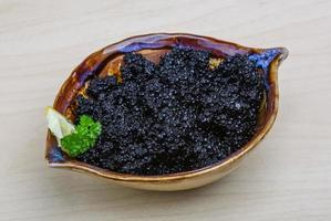 caviale nero in una ciotola su fondo di legno foto