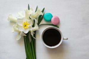 mattina caffè, macaron e giunchiglie su un' bianca tavola. composizione di un' mazzo di giunchiglie e tazze di caffè. foto