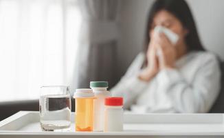 medicinali e bicchiere d'acqua con donna malata in background foto