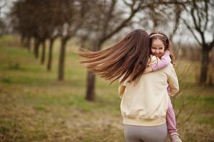 madre abbraccio sua bambino ragazza figlia nel primavera giardino. foto