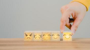 clienti mano seleziona un' smiley viso su un' di legno cubo bloccare 5 stella soddisfazione. migliore grande attività commerciale Servizi Vota il cliente Esperienza. soddisfazione sondaggio concetto. foto