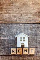 casa modello giocattolo in miniatura con iscrizione lettere di affitto parola su sfondo di legno foto