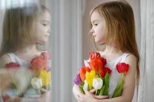 adorabile bambina con i tulipani vicino alla finestra