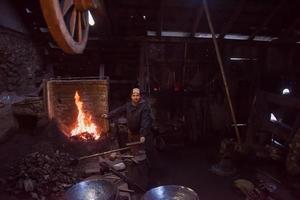 giovane tradizionale maniscalco Lavorando con Aperto fuoco foto