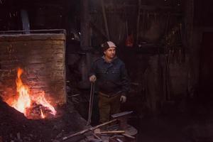 giovane tradizionale maniscalco Lavorando con Aperto fuoco foto