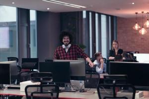 un' giovane uomo con un afro taglio di capelli sta nel un' moderno ufficio circondato di computer foto