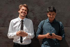 casuale multietnico avviare attività commerciale uomini uno di loro è indiano utilizzando smartphone durante rompere a partire dal opera nel davanti di grigio parete al di fuori foto