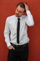 ritratto di avviare uomo d'affari nel un' bianca camicia con un' nero cravatta in piedi nel davanti di rosso parete al di fuori foto