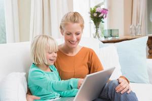 felice madre e figlia sul divano con laptop foto