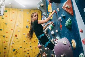 giovane donna arrampicata un' alto, interno, artificiale roccia arrampicata parete foto