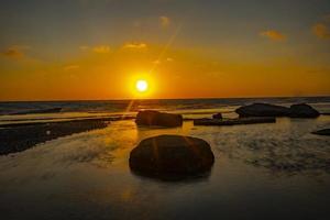 lungo esposizione fotografia di onde e ciottoli su spiaggia nel il tramonto foto