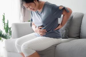 donna che soffre di mal di stomaco seduta sul divano di casa. dolore addominale, gastrite, ciclo mestruale. foto