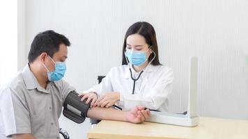 la dottoressa asiatica misura la pressione sanguigna di un paziente uomo utilizzando un misuratore di pressione sanguigna in ospedale mentre indossa una maschera medica contro l'infezione del sistema respiratorio. foto
