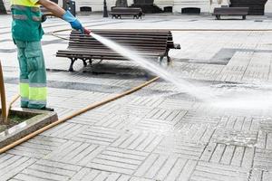 lavoratore pulizia un' città piazza con acqua utilizzando un' tubo flessibile. pubblico parco Manutenzione concetto. copia spazio foto