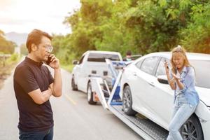 avvicinamento autista nel auto incidente utilizzando mobile Telefono con danneggiato auto camion scivoli su campagna e sole bagliore sfondo. foto