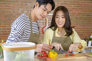 giovane sorridente asiatico coppia indossare un grembiule nel il cucina camera, cucinando concetto foto