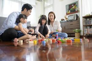 asiatico famiglia con bambini giocando e edificio Torre di colorato di legno giocattolo blocchi nel vivente camera a casa, educativo gioco. foto