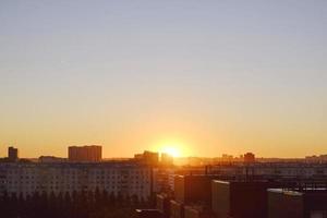 il sole sorge sopra il orizzonte illuminante il case e strade di il addormentato città foto