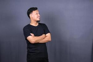 sorridente bello asiatico uomo nel nero maglietta in piedi con attraversato braccia isolato su grigio sfondo foto