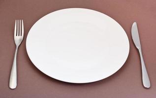 bianca porcellana piatto con forchetta e coltello su Marrone foto