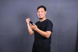 contento asiatico uomo Tenere un' smartphone e vincente il premio. isolato su grigio sfondo foto
