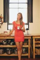 attraente giovane donna in cucina con una tazza di caffè foto