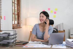 donna asiatica d'affari che utilizza smartphone per fare finanza matematica sulla scrivania di legno in ufficio, tasse, contabilità, concetto finanziario