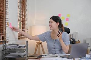 donna asiatica d'affari che utilizza smartphone per fare finanza matematica sulla scrivania di legno in ufficio, tasse, contabilità, concetto finanziario