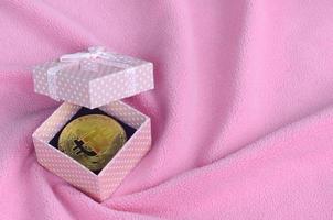 il d'oro bitcoin bugie nel un' piccolo rosa regalo scatola con un' piccolo arco su un' coperta fatto di morbido e soffice leggero rosa vello tessuto con un' grande numero di sollievo pieghe foto