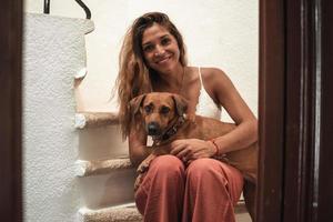 ritratto di bellissimo latina donna abbracciare sua cane tutti e due guardare a il telecamera. foto