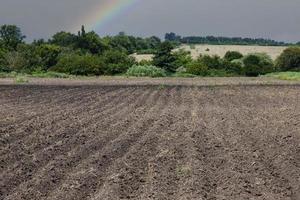 modello di righe nel arabile terra contro il sfondo di un' arcobaleno e un' piovoso cielo. foto