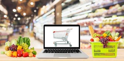 supermercato corridoio sfocato sfondo con il computer portatile computer e shopping carrello su legna tavolo drogheria in linea concetto foto