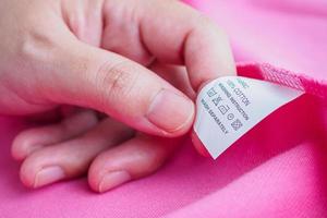 donna lettura su lavanderia cura lavaggio Istruzioni Abiti etichetta su rosa cotone camicia foto